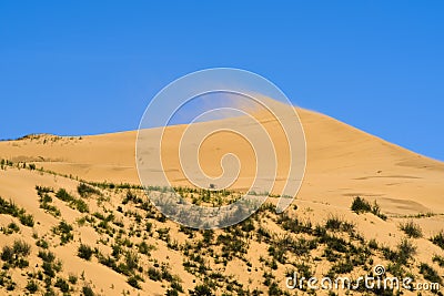 Dune against the background of a bright blue sky. The wind blows the sand off the ridge of the dune Stock Photo